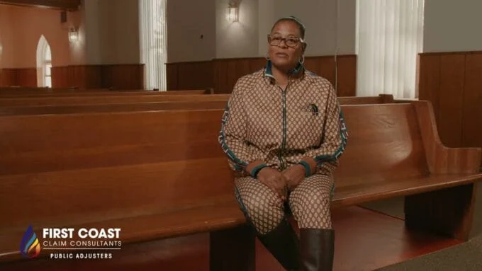A woman sitting alone on a wooden church pew, smiling and looking to the side.