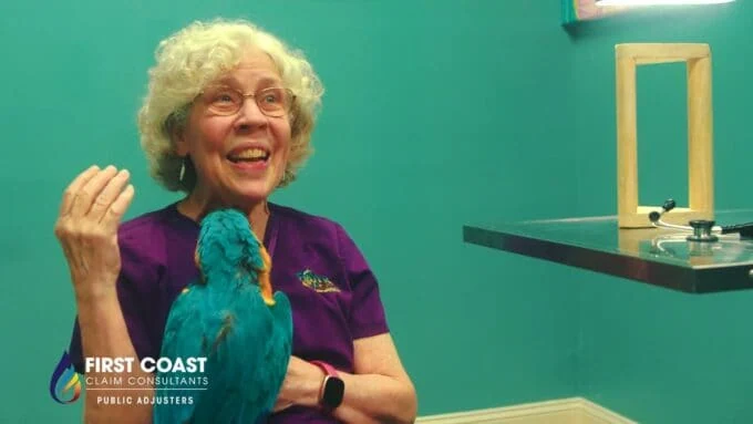 A woman with curly gray hair smiling and holding a colorful puppet bird.